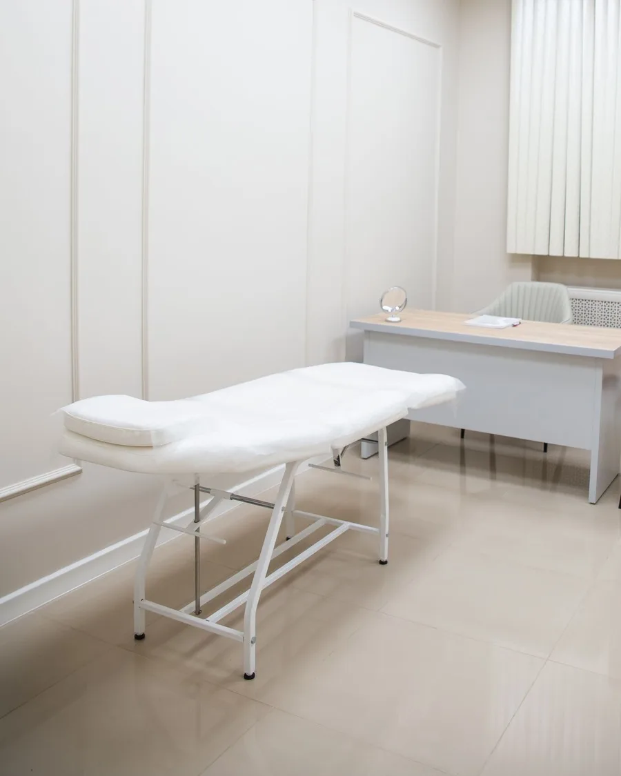 Salle de soins du cabinet: table de kinésithérapie prête et bureau, dans une pièce claire